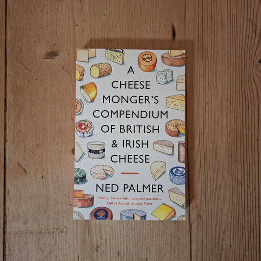 A book titled 'A Cheese Monger's Compendium of British & Irish Cheese' by Ned Palmer, featuring a white cover decorated with colorful illustrations of various cheeses, placed flat on a rustic wooden surface.