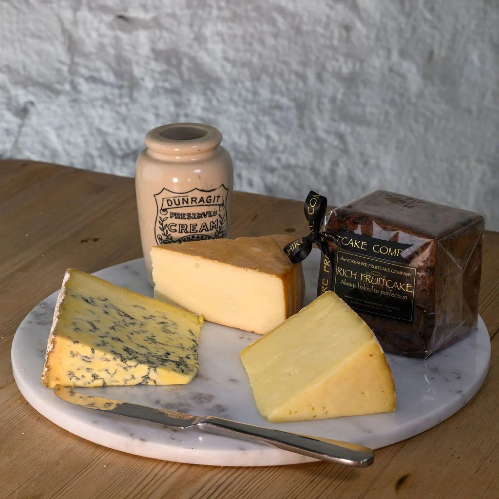 Three types of cheese on a marble board and a box of 'Rich Fruitcake' on a wooden surface.