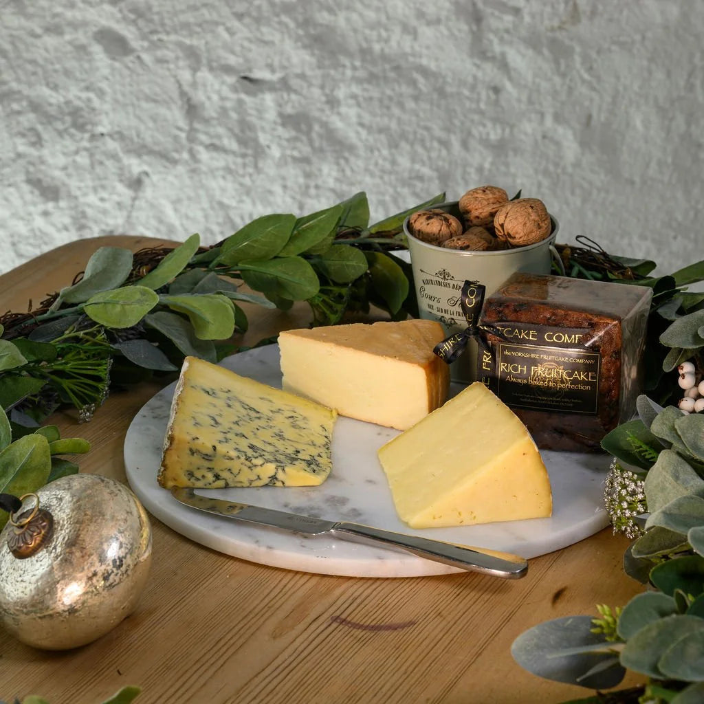 Assorted cheeses, yorkshire fruitcake, on a marble board with decorative elements on a wooden table.