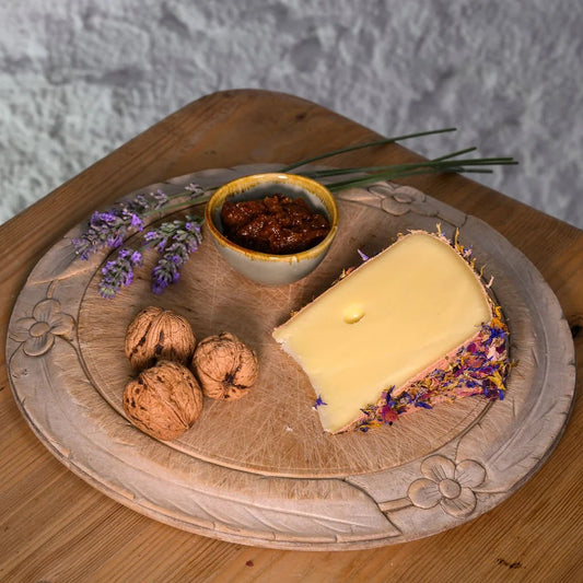 Alp Blossom cheese with flowers, walnuts, and a small bowl of jam on a wooden board.