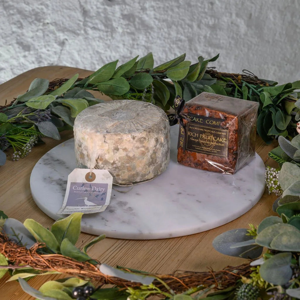 Yoredale round of cheese and a yorkshire fruitcake on a marble platter with greenery around