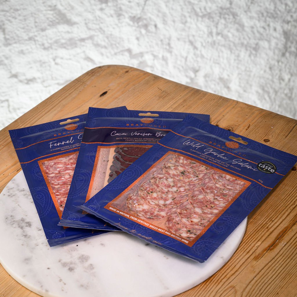 Three packages of bray cured charcuterie on a marble and wooden surface