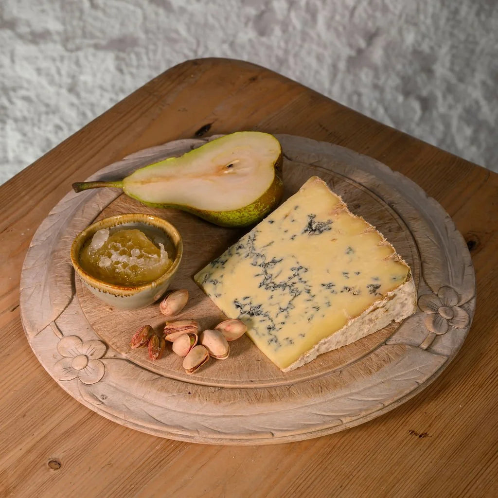 Platter with colston bassett blue cheese, pear, nuts, and a small dish on a wooden surface.