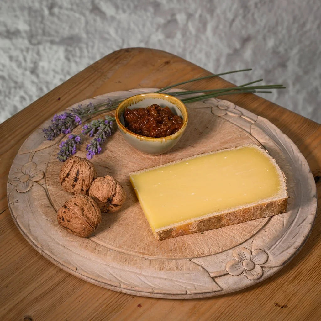 Cheese platter with comte cheese, walnuts, and a small bowl of chutney on a wooden board.