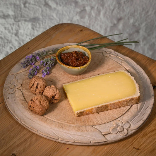 Cheese platter with comte cheese, walnuts, and a small bowl of chutney on a wooden board.
