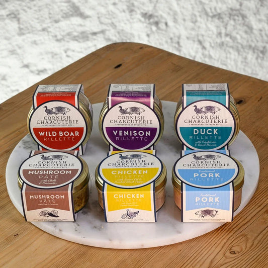 Assorted rillettes from Cornish Charcuterie on a marble platter with a wooden surface and textured wall background.