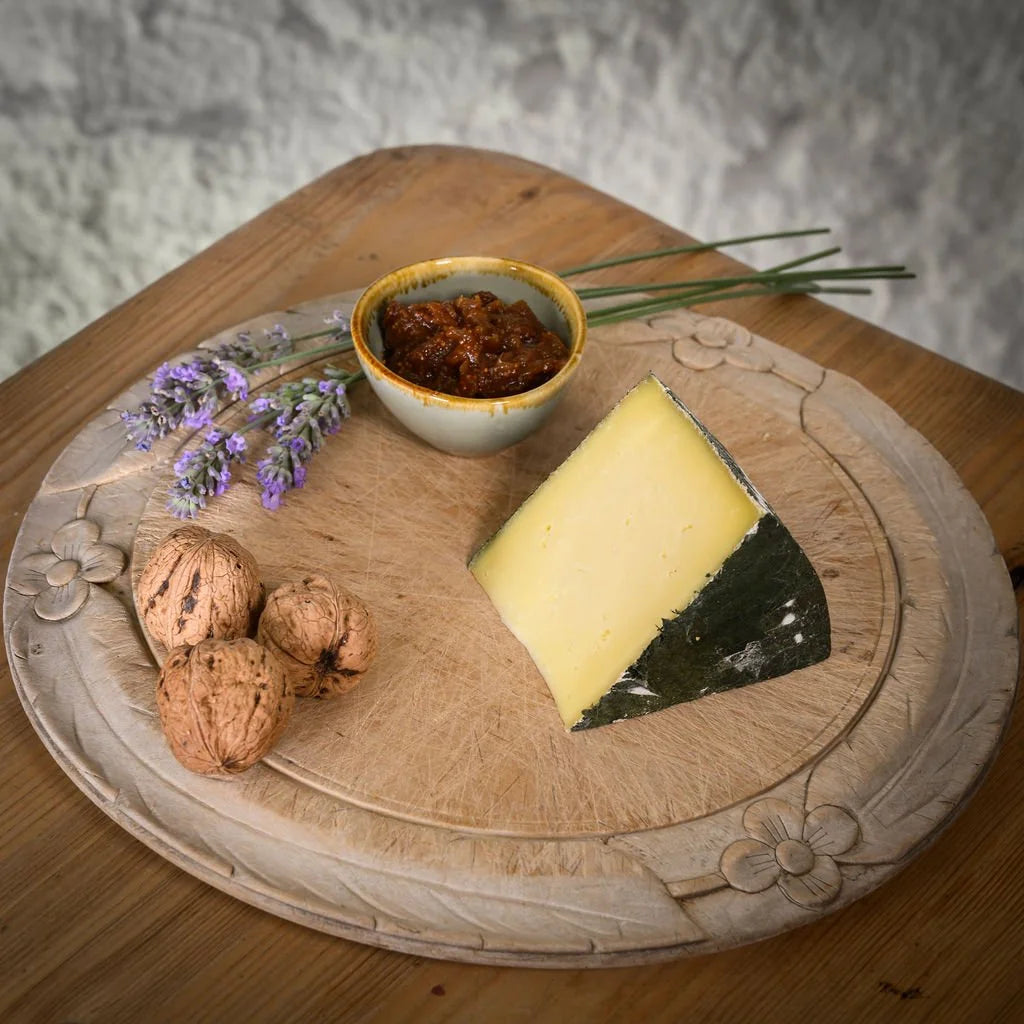 Cheese platter with a wedge of cornish yarg cheese, walnuts, a small bowl of chutney, and lavender on a wooden board.