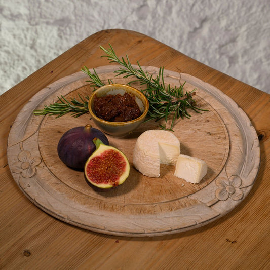 Wooden platter with figs, Crottin, and a small bowl of jam on a wooden surface.