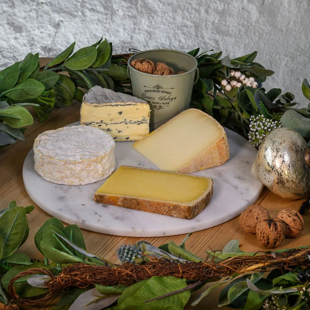 Assorted cheeses on a marble platter with decorative elements on a wooden surface.