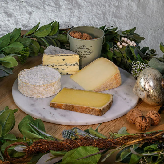Assorted cheeses on a marble platter with decorative elements on a wooden surface.