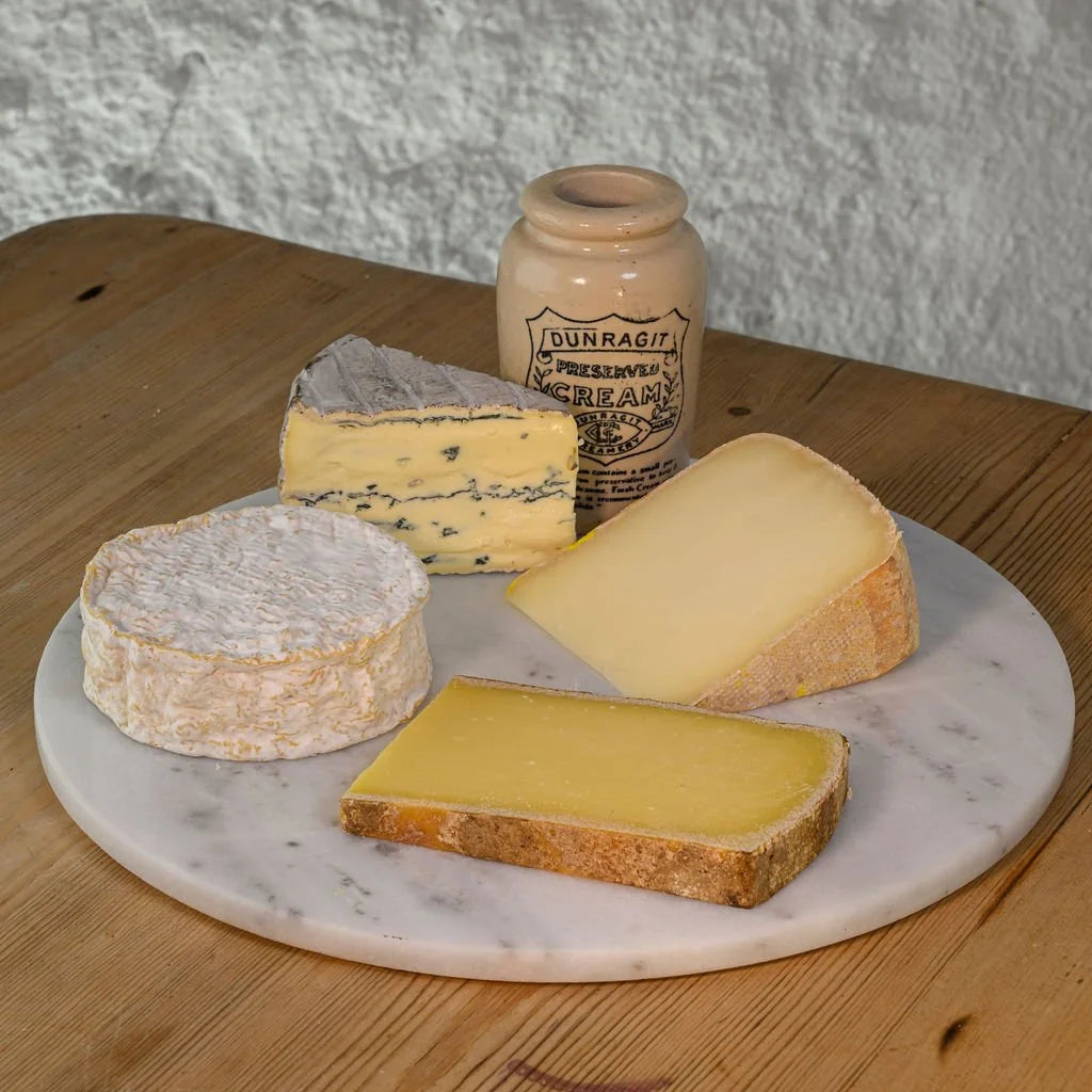Assorted cheeses on a marble board with a vintage jar labeled 'Dunragit' on a wooden surface.
