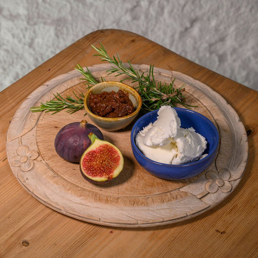 Wooden board with figs, a bowl of Helwith Goats' cheese, on a wooden surface.