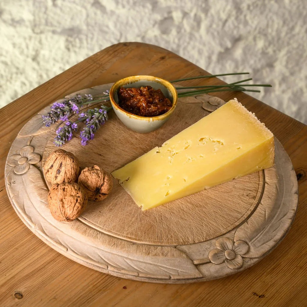 isle of mull cheddar wedge on a wooden board with nuts, herbs, and a small bowl of chutney.