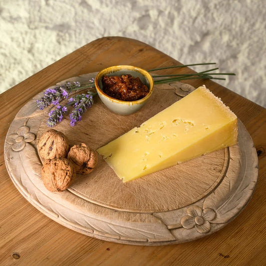 isle of mull cheddar wedge on a wooden board with nuts, herbs, and a small bowl of chutney.