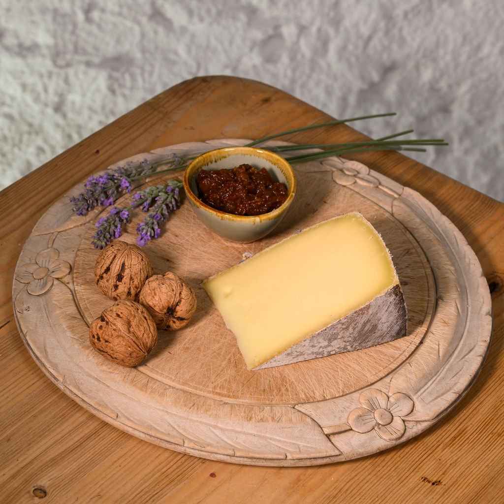 Cheese platter with kaltbach creamy cheese, nuts, and a small bowl on a wooden board.