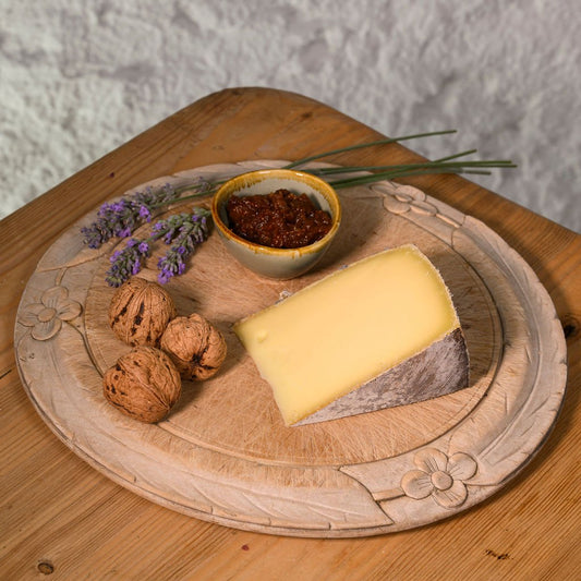 Cheese platter with kaltbach creamy cheese, nuts, and a small bowl on a wooden board.