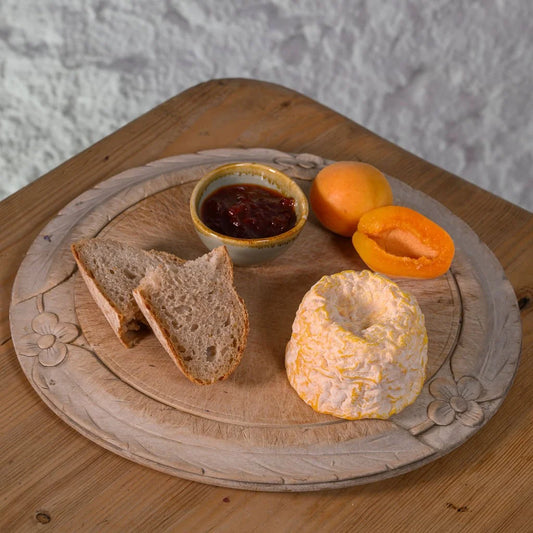 Wooden plate with Langres cheese, bread, jam, and apricots on a textured surface