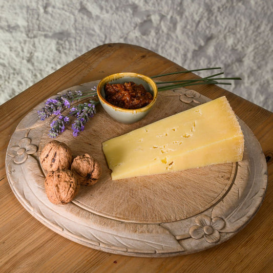 Cheese platter with a wedge of lincolnshire poacher cheese, nuts, and a small bowl on a wooden board.