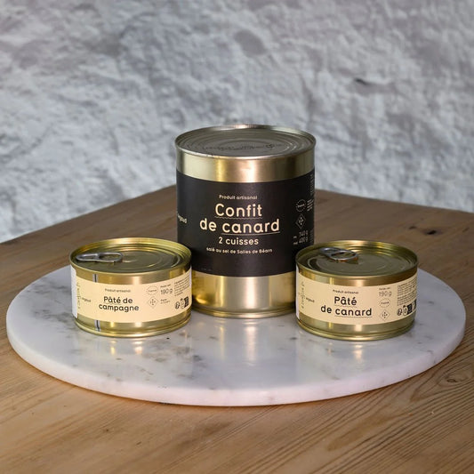 Three tins of duck confit on a marble tray with a gray textured wall background.