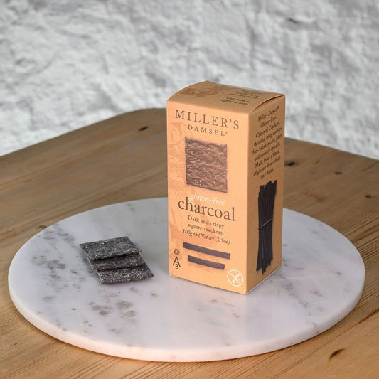 Box of Miller's Damsel charcoal gluten free crackers on a marble coaster with crackers beside it.