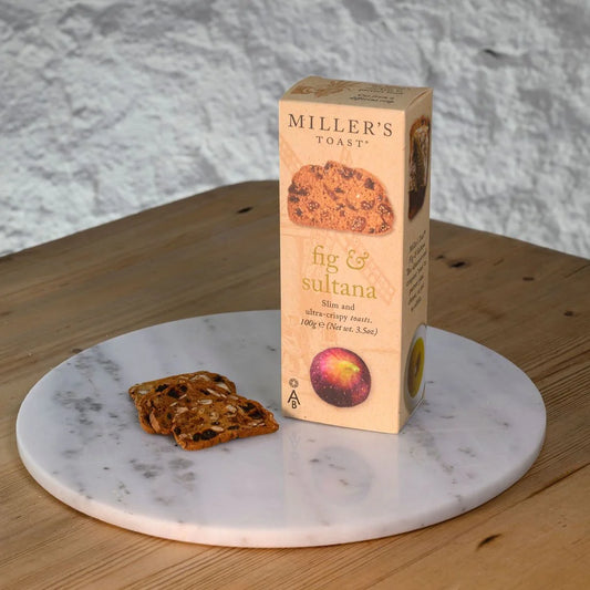 Box of Miller's Toast fig & sultana toast on a marble platter with slices of toast.