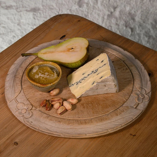 Cheese platter with a wedge of montagnolo cheese, half a pear, nuts, and a small dish on a wooden board.
