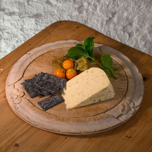 Wooden board with a wedge of northumberland nettle cheese, crackers, and small fruits on a textured wall background