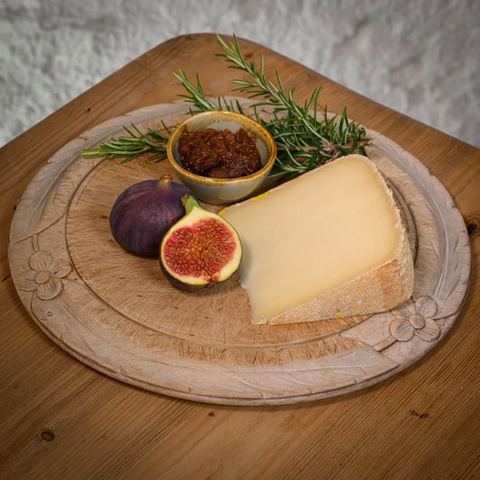 Cheese platter with a wedge of ossau iraty, figs, and a small bowl of jam on a wooden board.