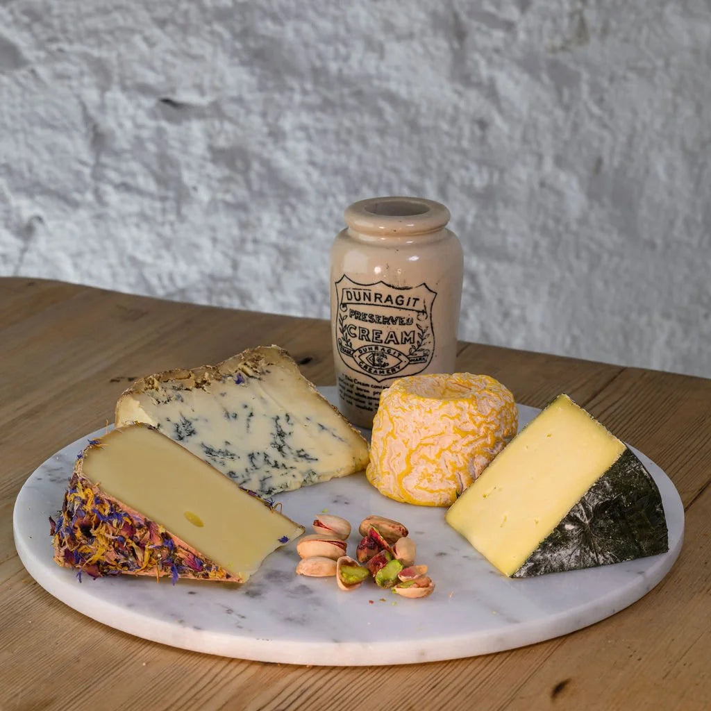 Assorted cheeses on a marble platter with a jar of cream in the background.