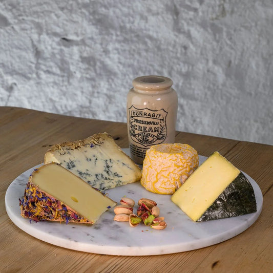 Assorted cheeses on a marble platter with a jar of cream in the background.