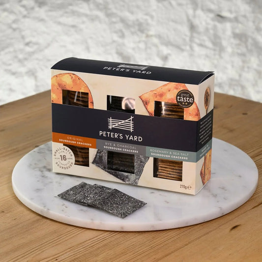 Box of Peter's Yard crackers on a marble platter with a wooden surface and gray wall background