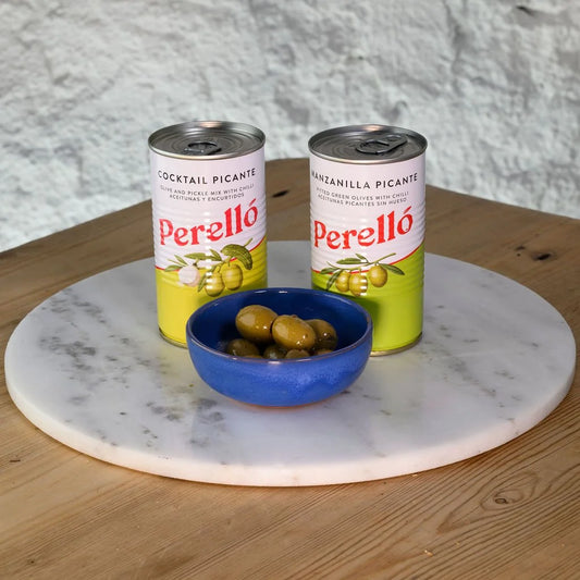 Two cans of Perello olives on a marble tray with a bowl of olives on a wooden surface.
