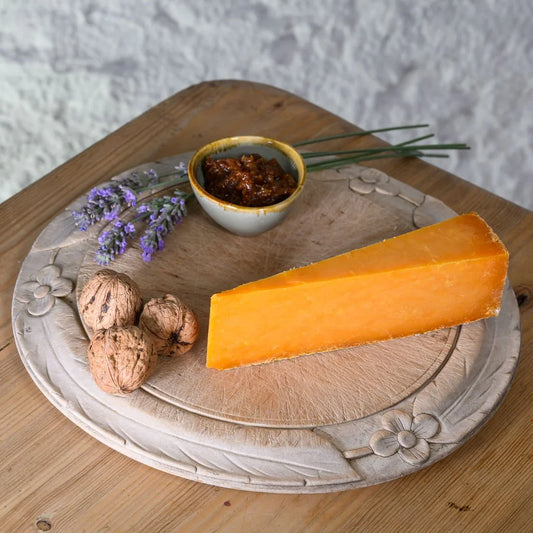 Triangle of Sparkenhoe Red Leicester cheese on a decorative plate with walnuts, a small bowl, and lavender flowers.