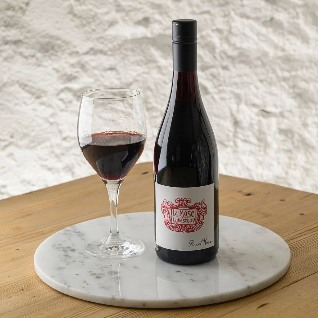 Bottle of red wine and a glass on a marble coaster with a textured wall background