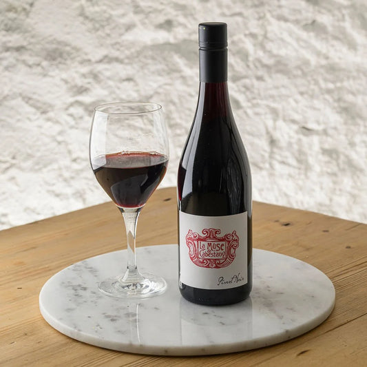 Bottle of red wine and a glass on a marble coaster with a textured wall background