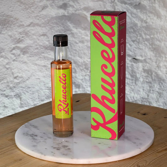 Bottle and box of Rhucello on a marble surface with a textured gray background
