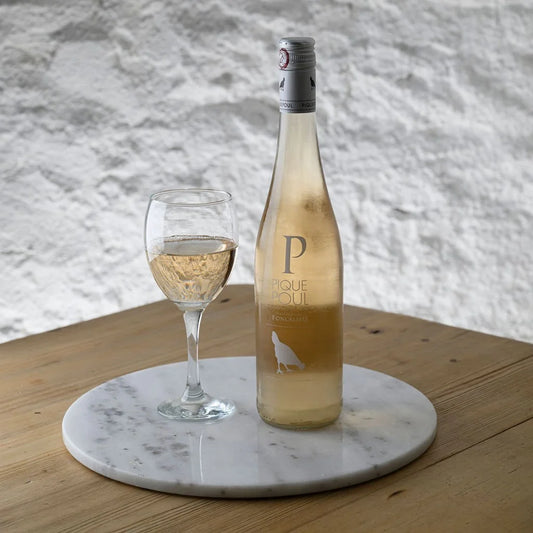 Bottle of rose wine with a glass on a marble coaster against a textured wall.