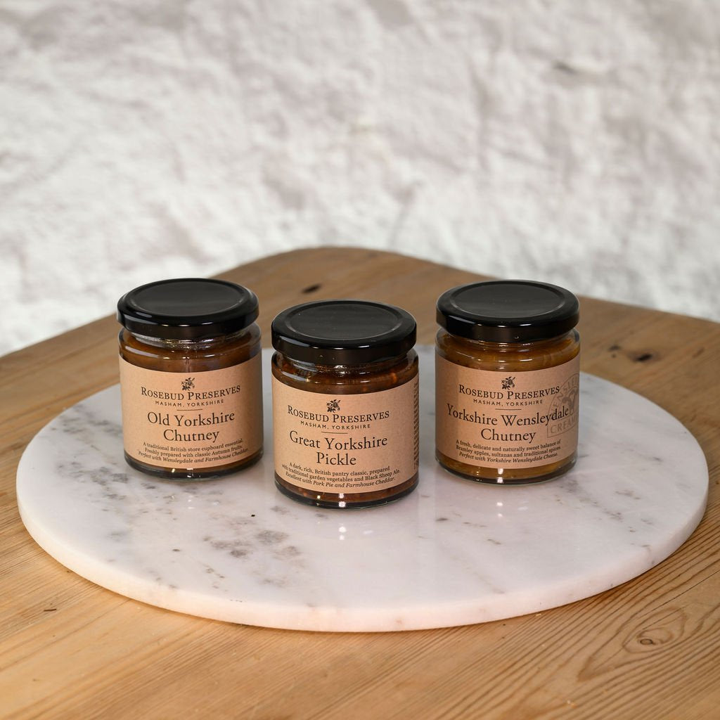 Three jars of Rosebud Preserves on a marble platter with a wooden surface and white textured background.