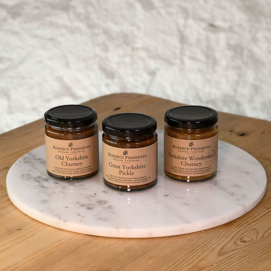 Three jars of Rosebud Preserves on a marble platter with a wooden surface and white textured background.