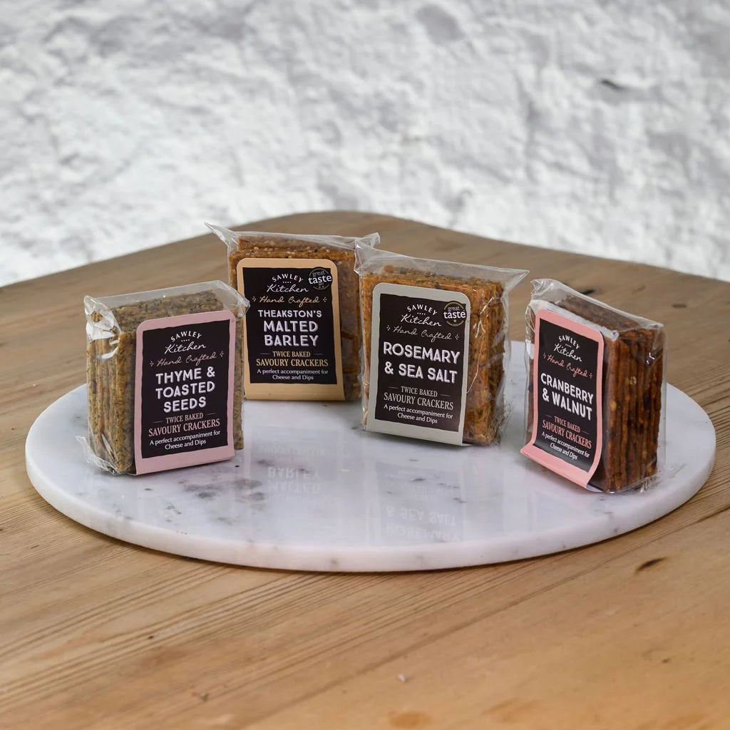 Assorted packages of sawley kitchen crackers on a marble platter with a wooden surface and gray textured background.