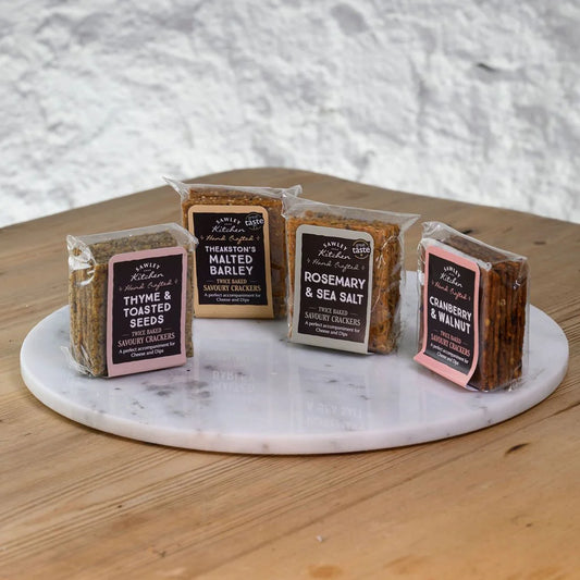 Assorted packages of sawley kitchen crackers on a marble platter with a wooden surface and gray textured background.