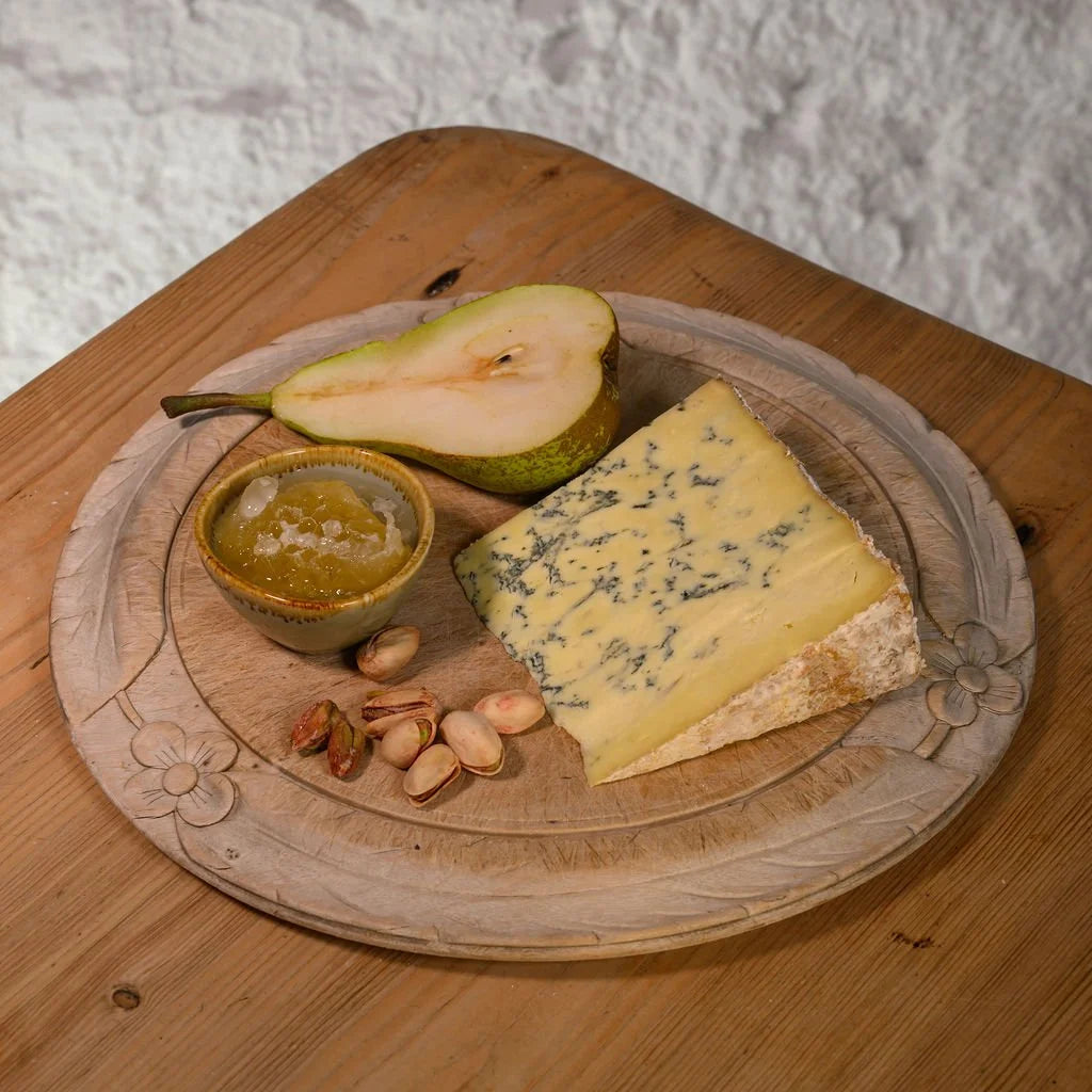 Platter with Swaledale blue cheese, pear, nuts, and a small dish on a wooden surface.