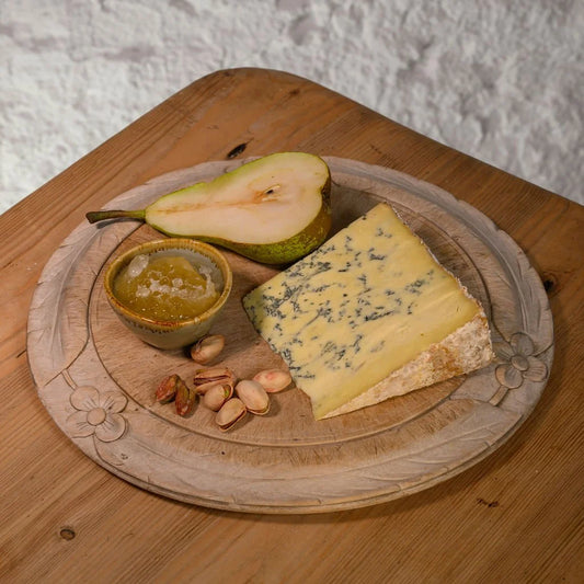 Platter with Swaledale blue cheese, pear, nuts, and a small dish on a wooden surface.