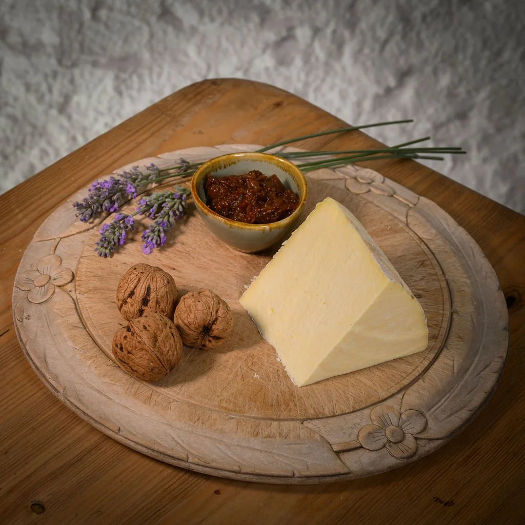 Swaledale cheese, nuts, and a small bowl of spread on a decorative wooden board with a textured background.