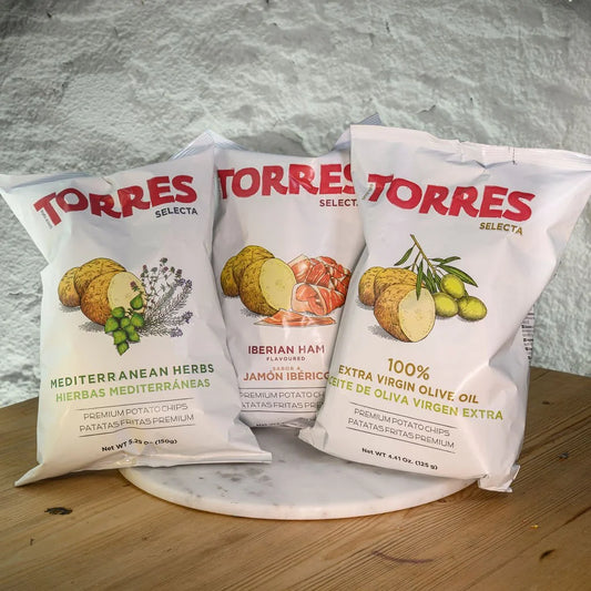 Three packages of Torres Selecta crisps on a marble surface with a grey background