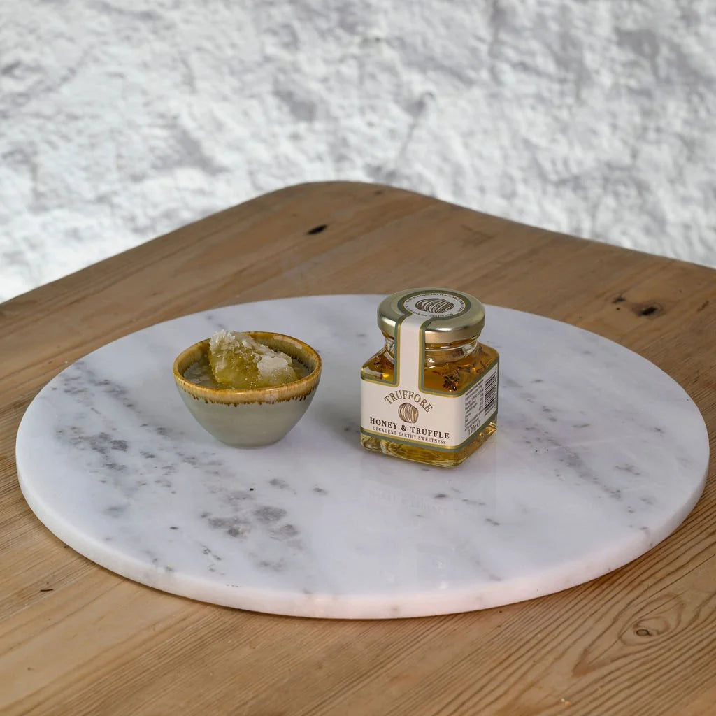 Jar of Truffle honey on a marble platter with a small bowl on a wooden surface.