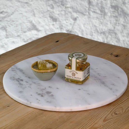 Jar of Truffle honey on a marble platter with a small bowl on a wooden surface.