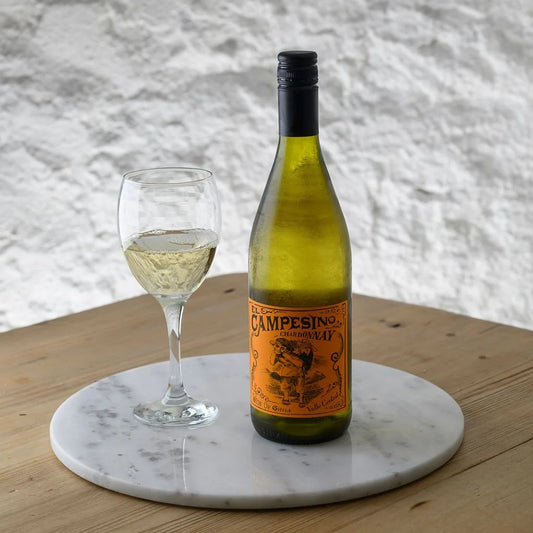 Bottle of El Campesino white wine with a glass on a marble coaster against a textured wall.