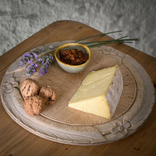 Triangle of Yoredale Wensleydale on a wooden board with walnuts and a small bowl of chutney.