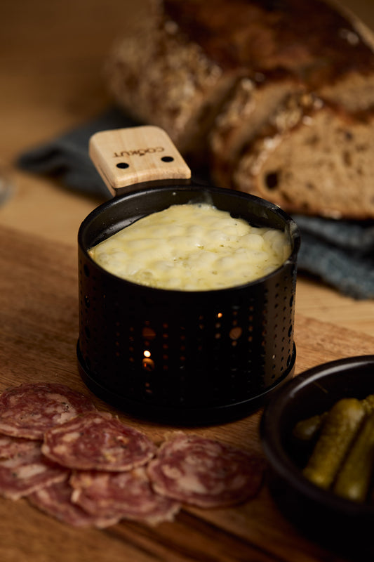 Melted raclette cheese with charcuterie, pickles and bread